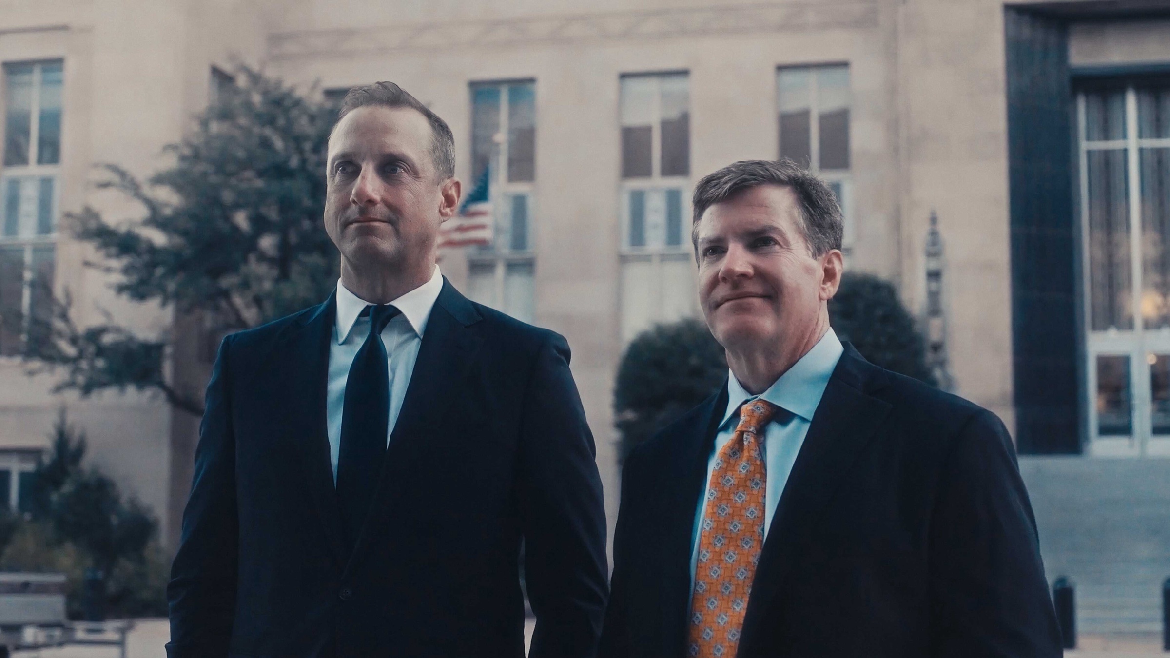 Two attorneys in suits standing outside a courthouse, a cinematic still from a Story First law firm video shoot