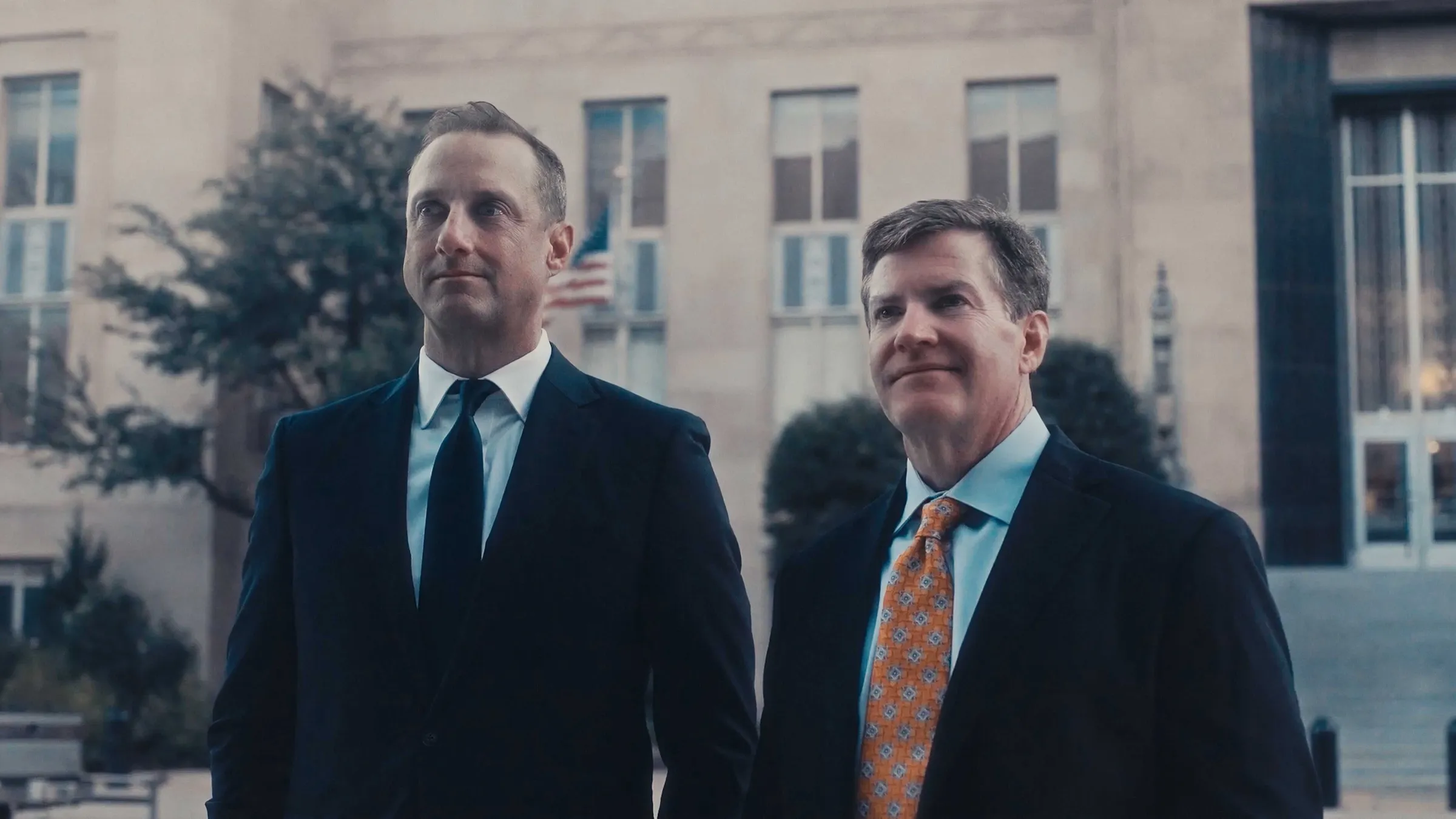 Two attorneys in suits standing outside a courthouse, a cinematic still from a Story First law firm video shoot