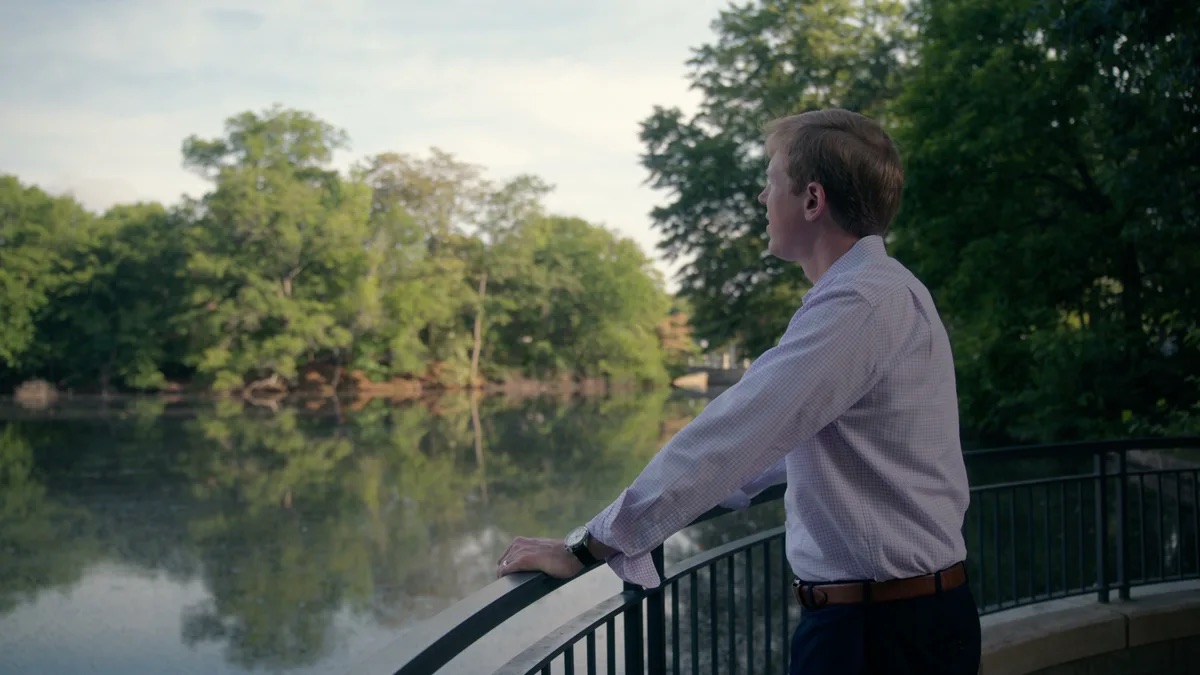 Kevin Patrick Law brand film thumbnail. A man in a button-down shirt stands at a black railing beside a lake with trees reflected in the water.