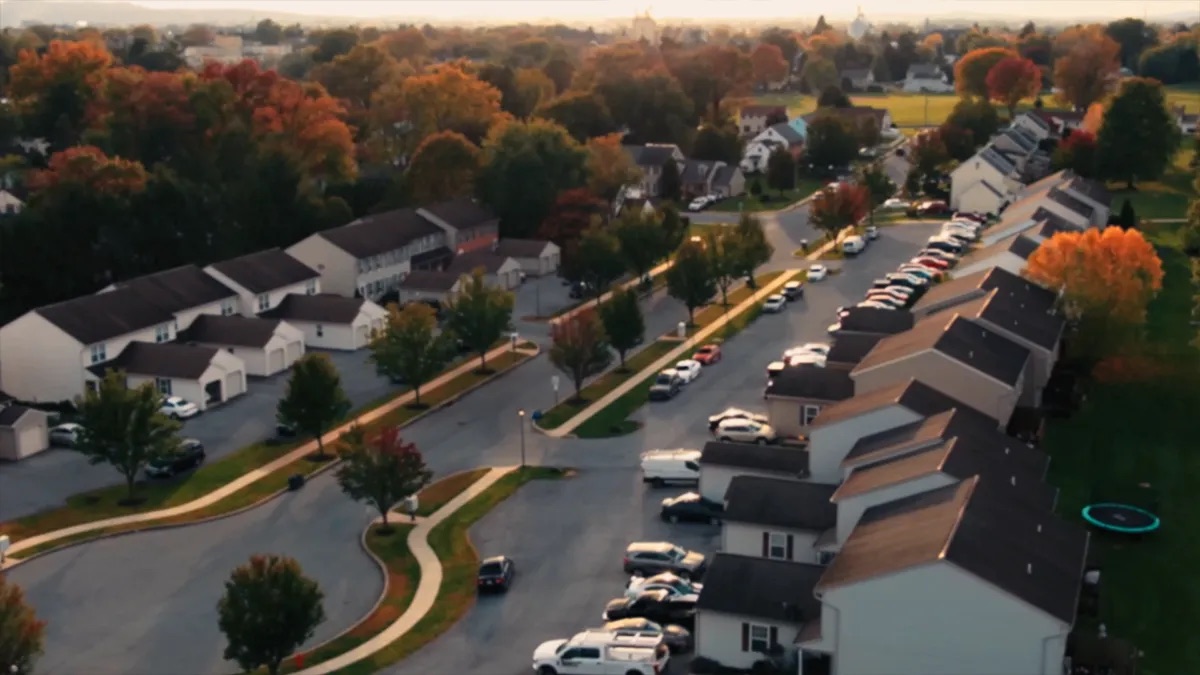 Practice area video thumbnail on condo and HOA claims. Aerial view of a residential neighborhood in autumn, rows of townhomes along a curved street, trees with orange and red leaves.