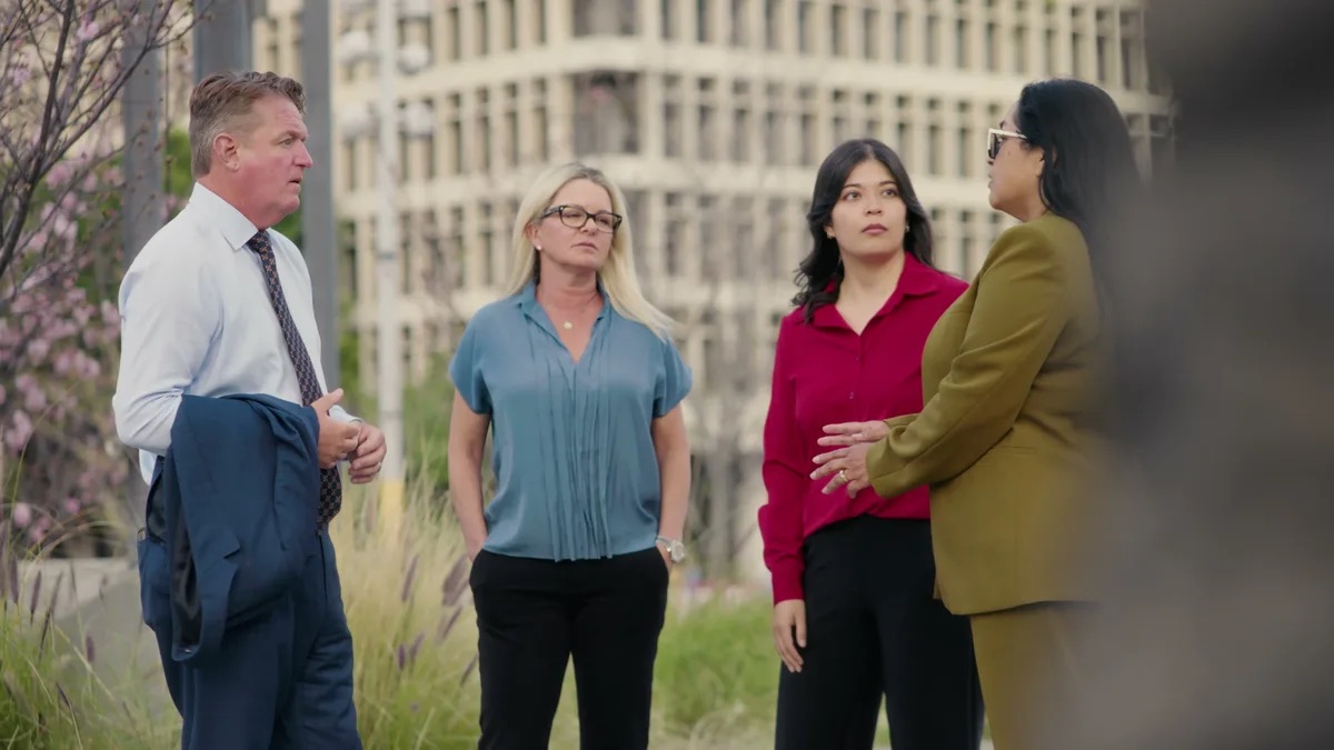 KMD Law practice area video thumbnail on negligent transmission of STDs. Four people in business clothes stand talking outside a downtown building, one gesturing while the rest listen.