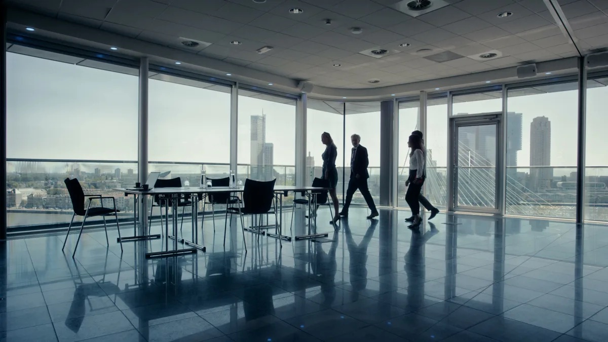 Padula Law practice area video thumbnail on general fraud. Three people in silhouette walk past floor to ceiling windows in an office conference room, tall buildings and a cable bridge outside.