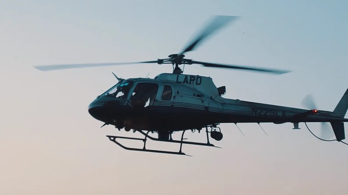 Practice area video thumbnail on police misconduct. An LAPD helicopter in flight against a light sky, the rotor blades blurred in motion.